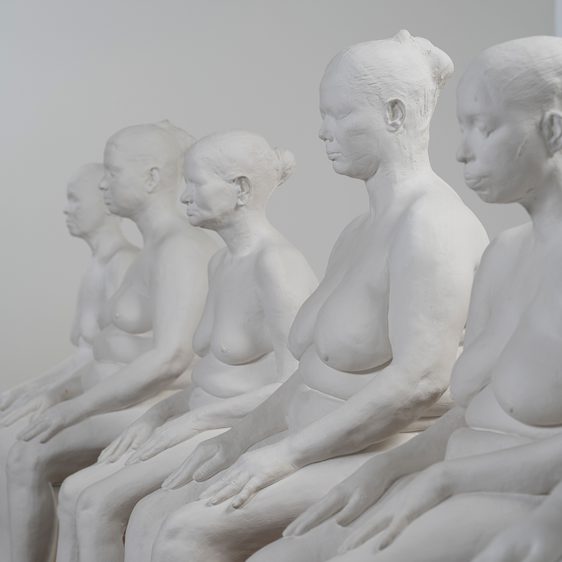 A row of white plaster casts of female seated nude figures.