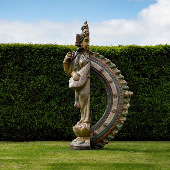 A sculpture of a female figure which has been cut in half vertically, with a semi-circular structure replacing the second half, viewed outdoors.