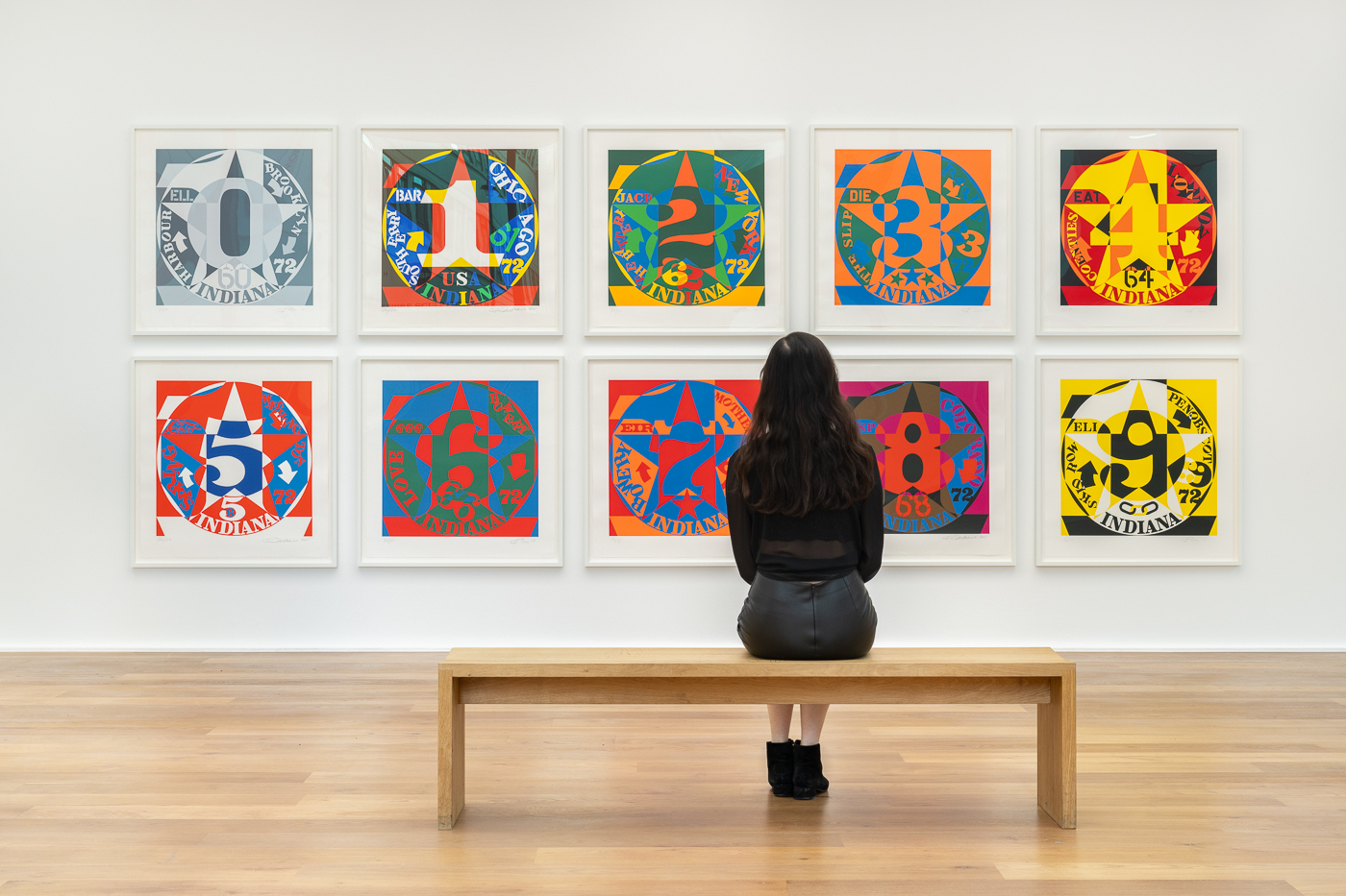 A woman sitting on a bench in front of a display of brightly coloured pop art prints in a gallery.