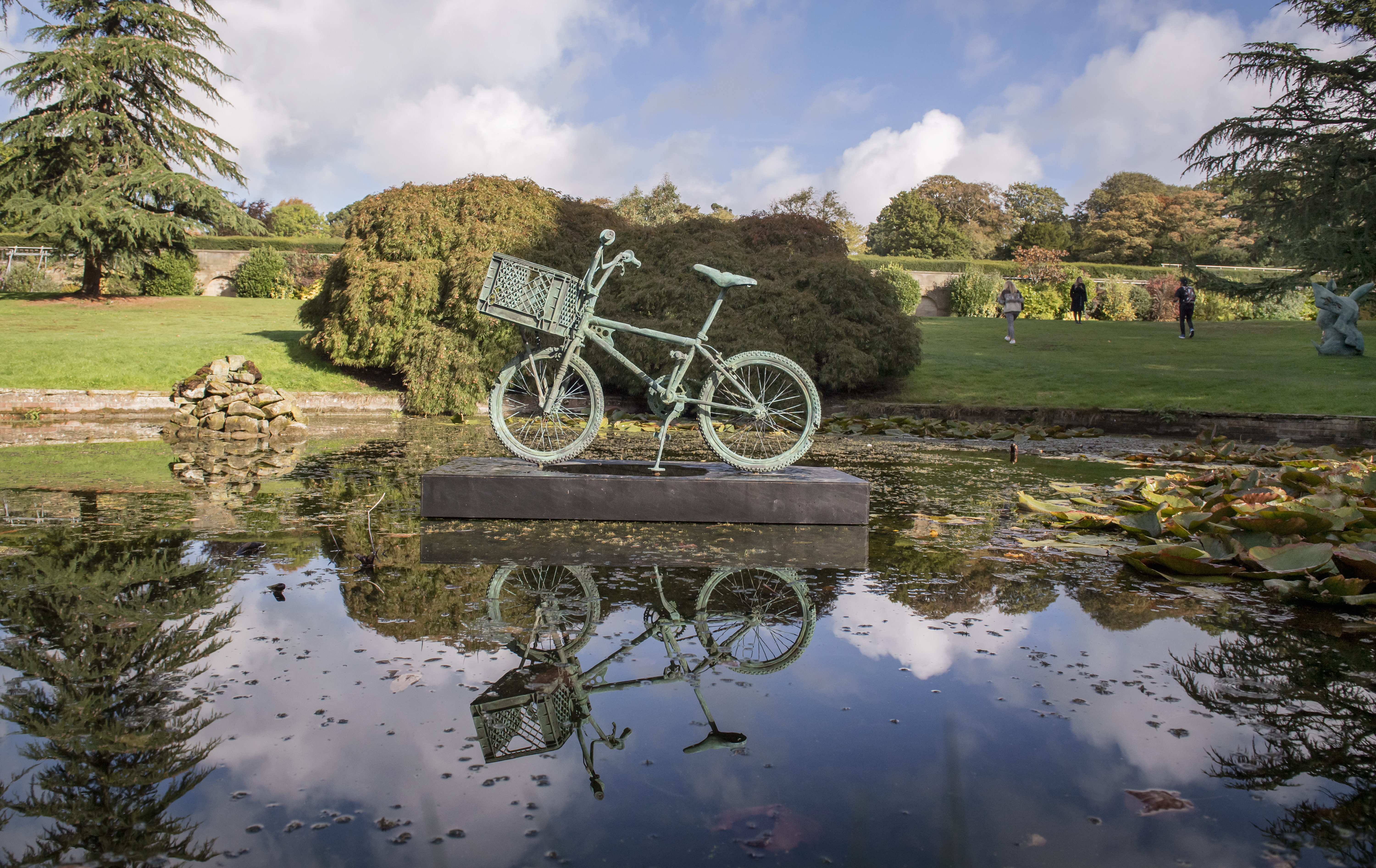 A bronze bicycle sculpture displayed on a plinth in the middle of a pond.