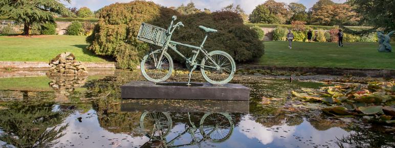 A bronze bicycle sculpture displayed on a plinth in the middle of a pond.