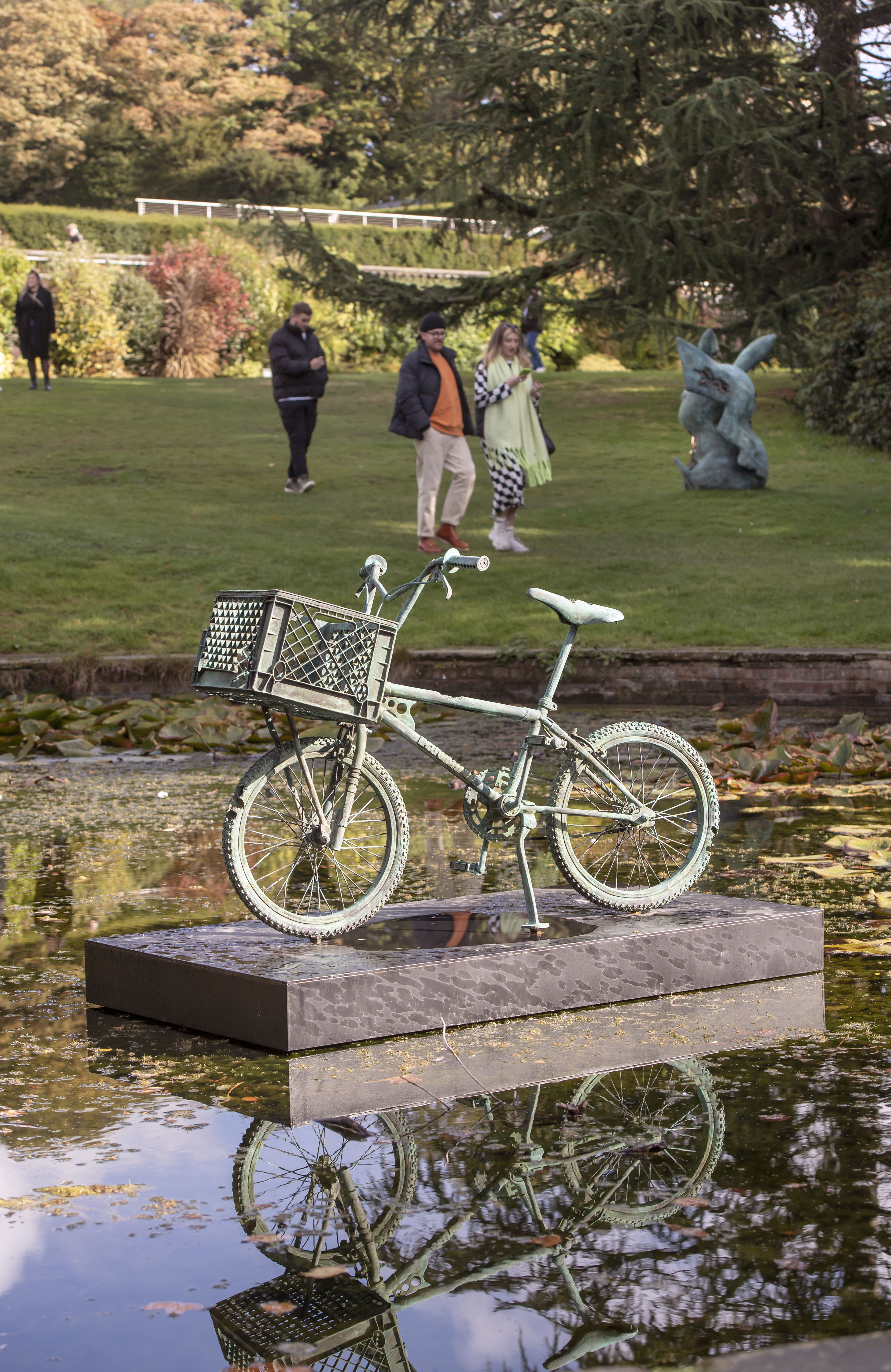A bronze bicycle sculpture displayed on a plinth in the middle of a pond.