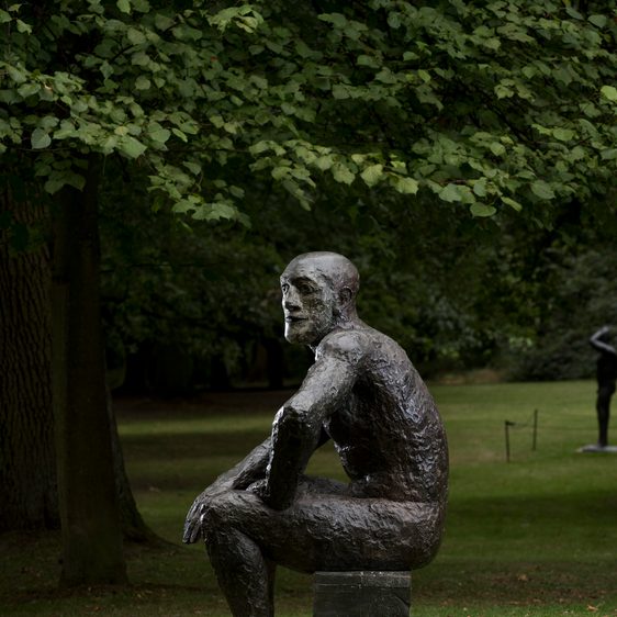 A bronze seated figure, displayed outdoors.