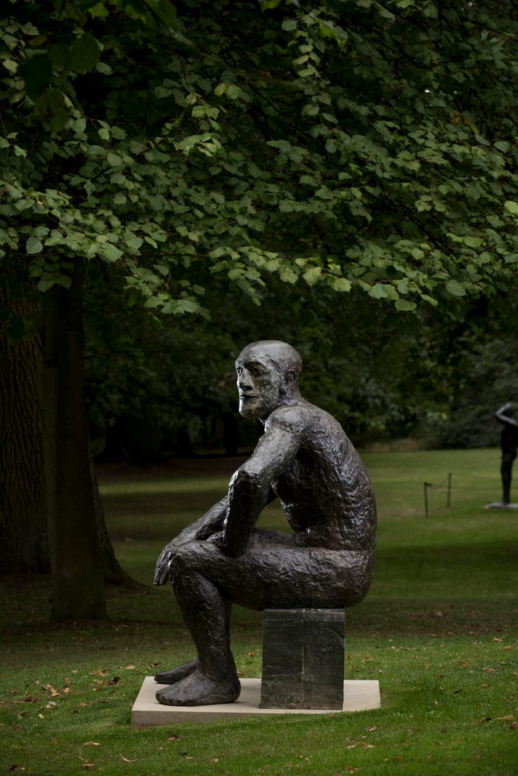 A bronze seated figure, displayed outdoors.