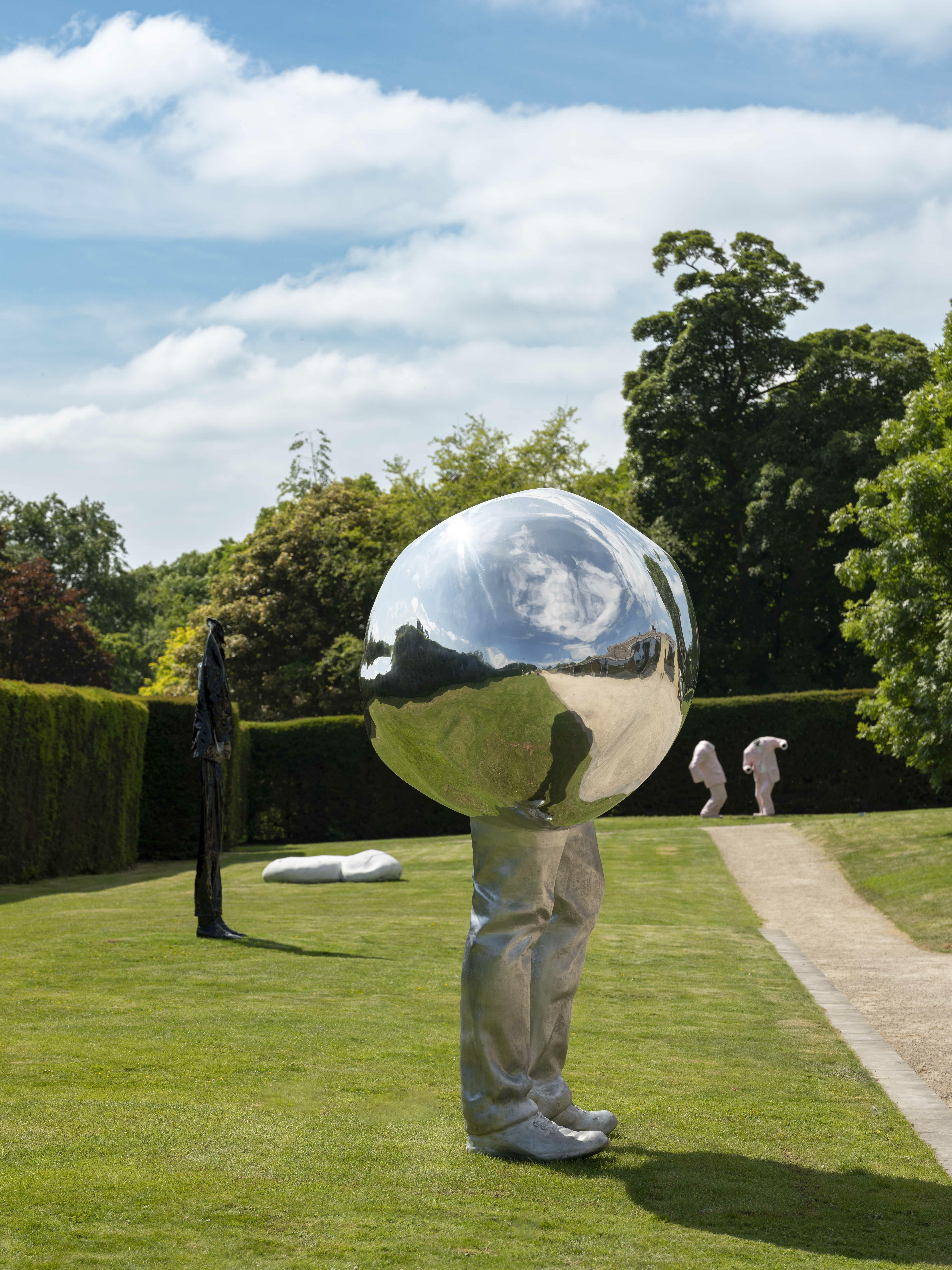 A silver sculpture with legs on the lawn and more sculptures in the background.