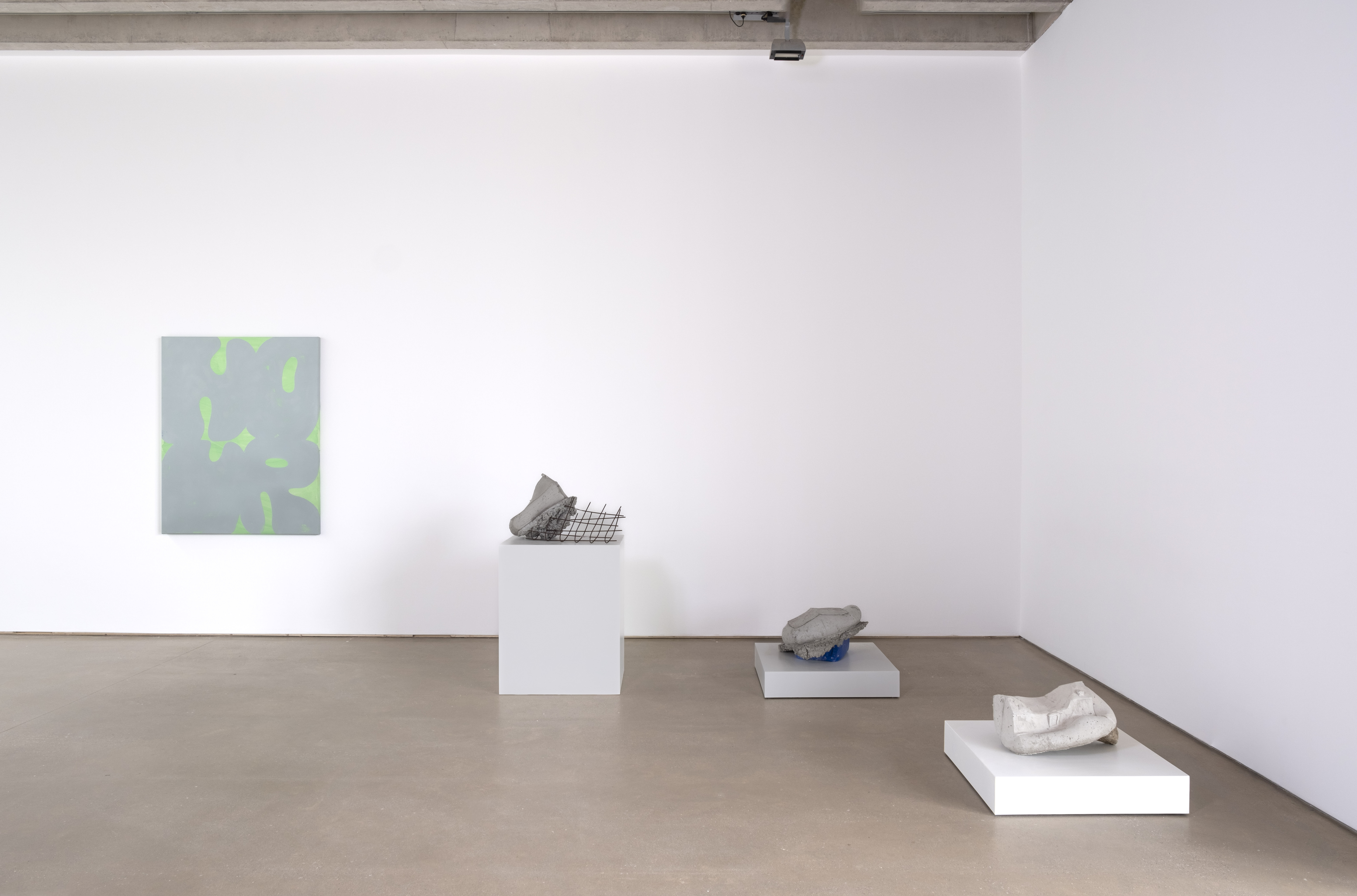 Three sculptures on plinths and a green and grey painting hung on the wall in a gallery