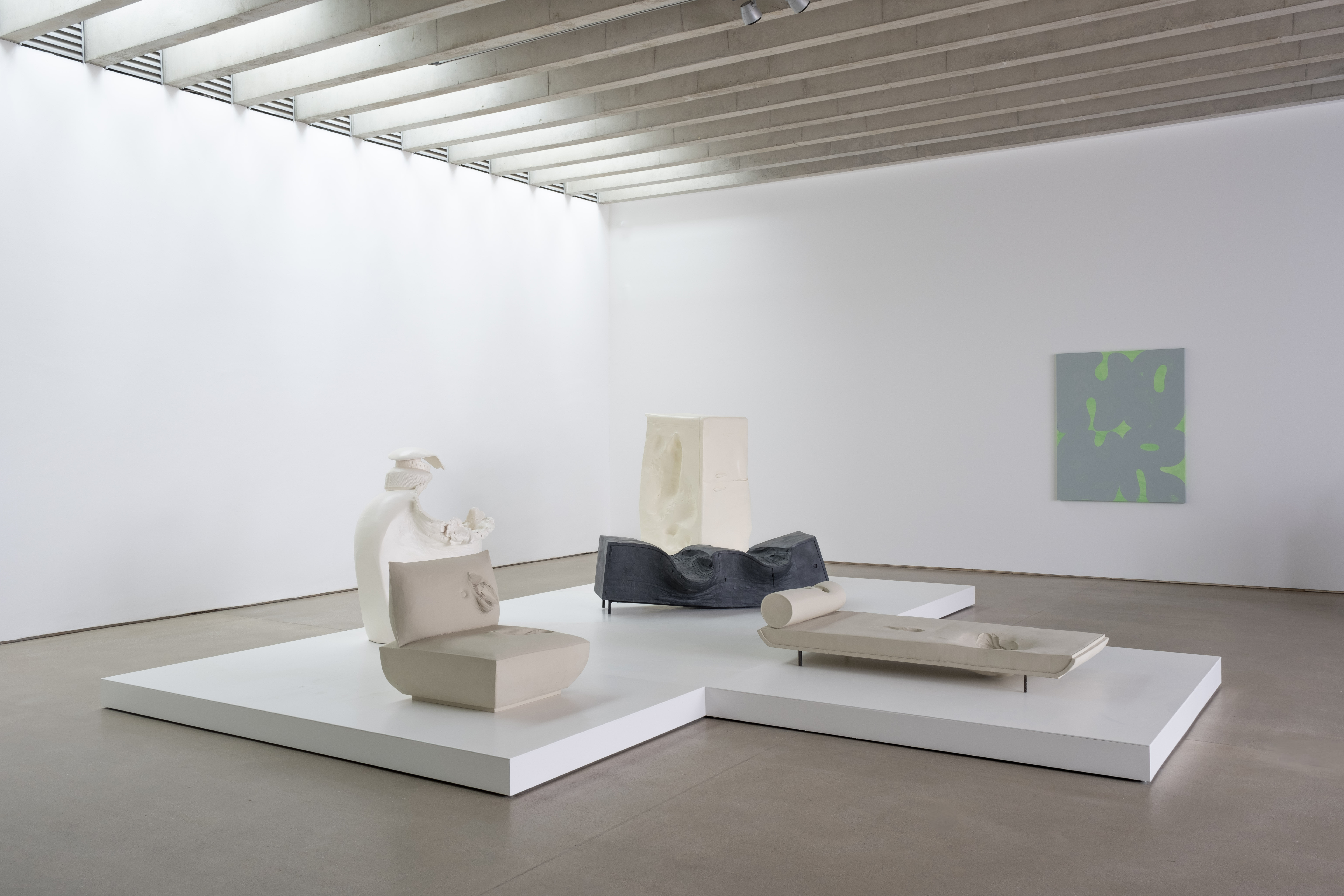 Five sculptures on a white plinth in a gallery and a canvas hung on the wall.