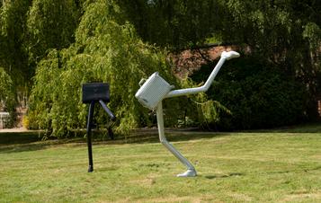 A silver suitcase sculpture and black briefcase sculpture both with legs on a lawn.