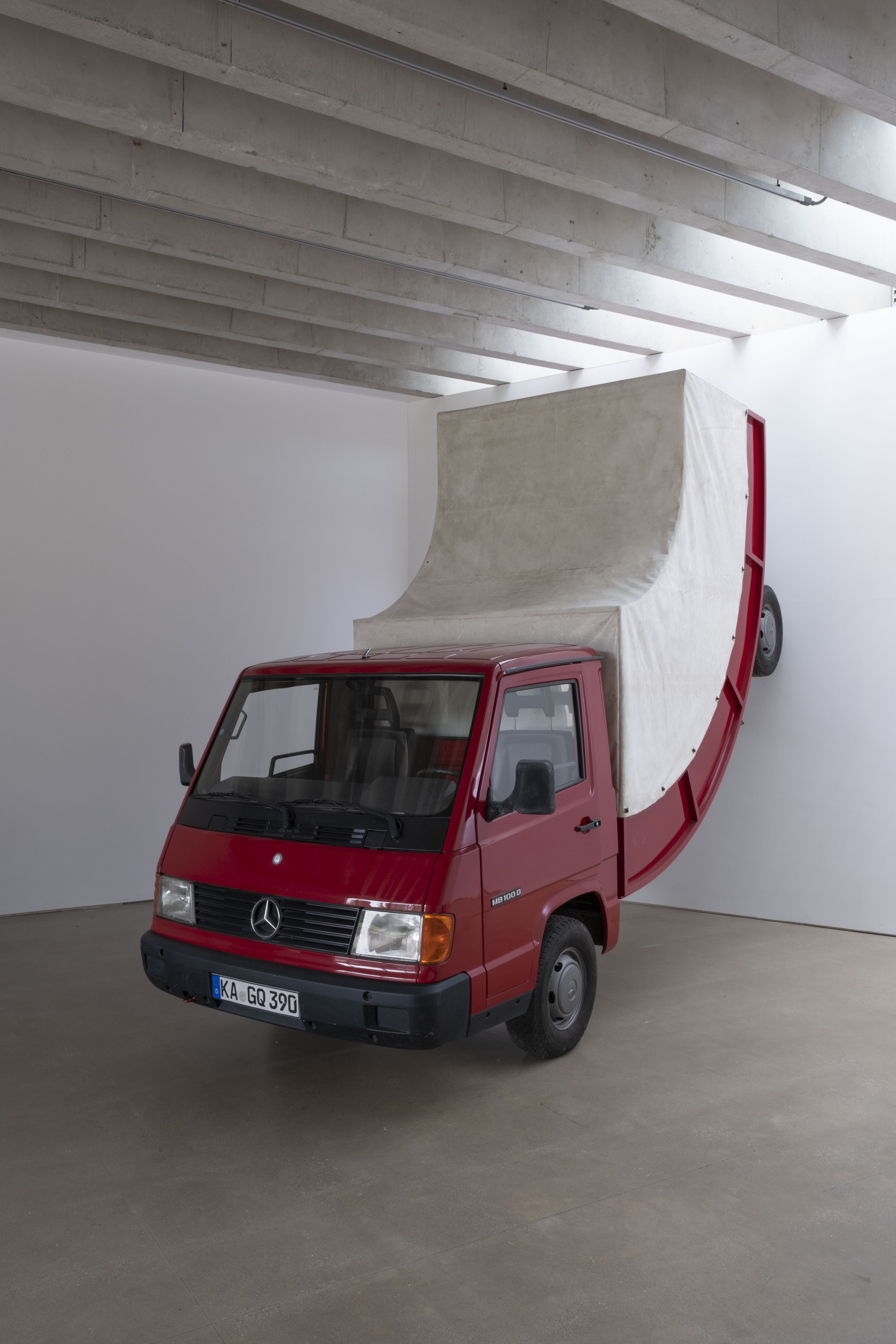 A bent red truck against a wall inside a gallery