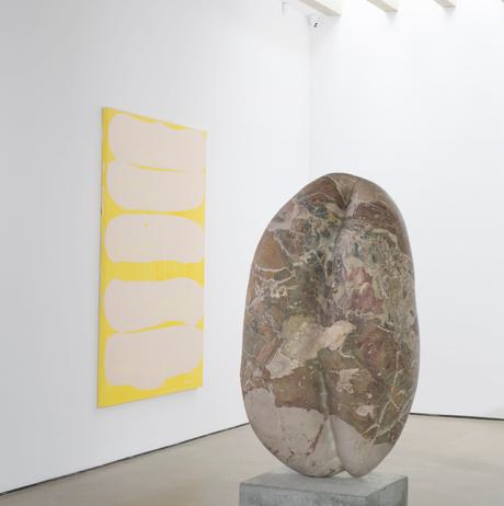 Stone sculpture and in the background a canvas hung on the wall in pink and yellow.