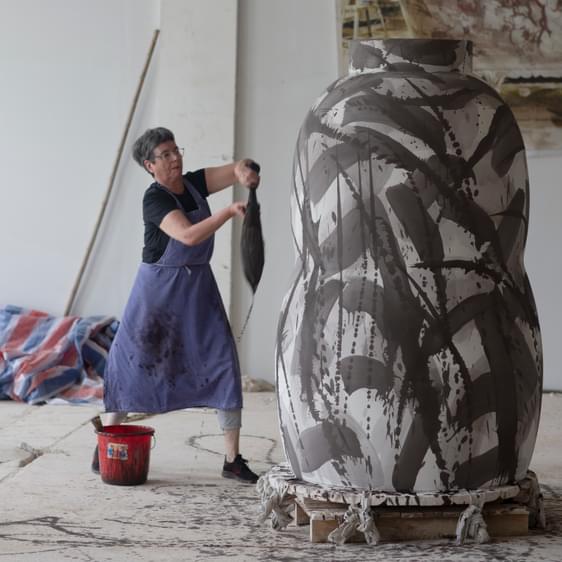 Woman painting a larger than life sized ceramic vase with big paintbrush