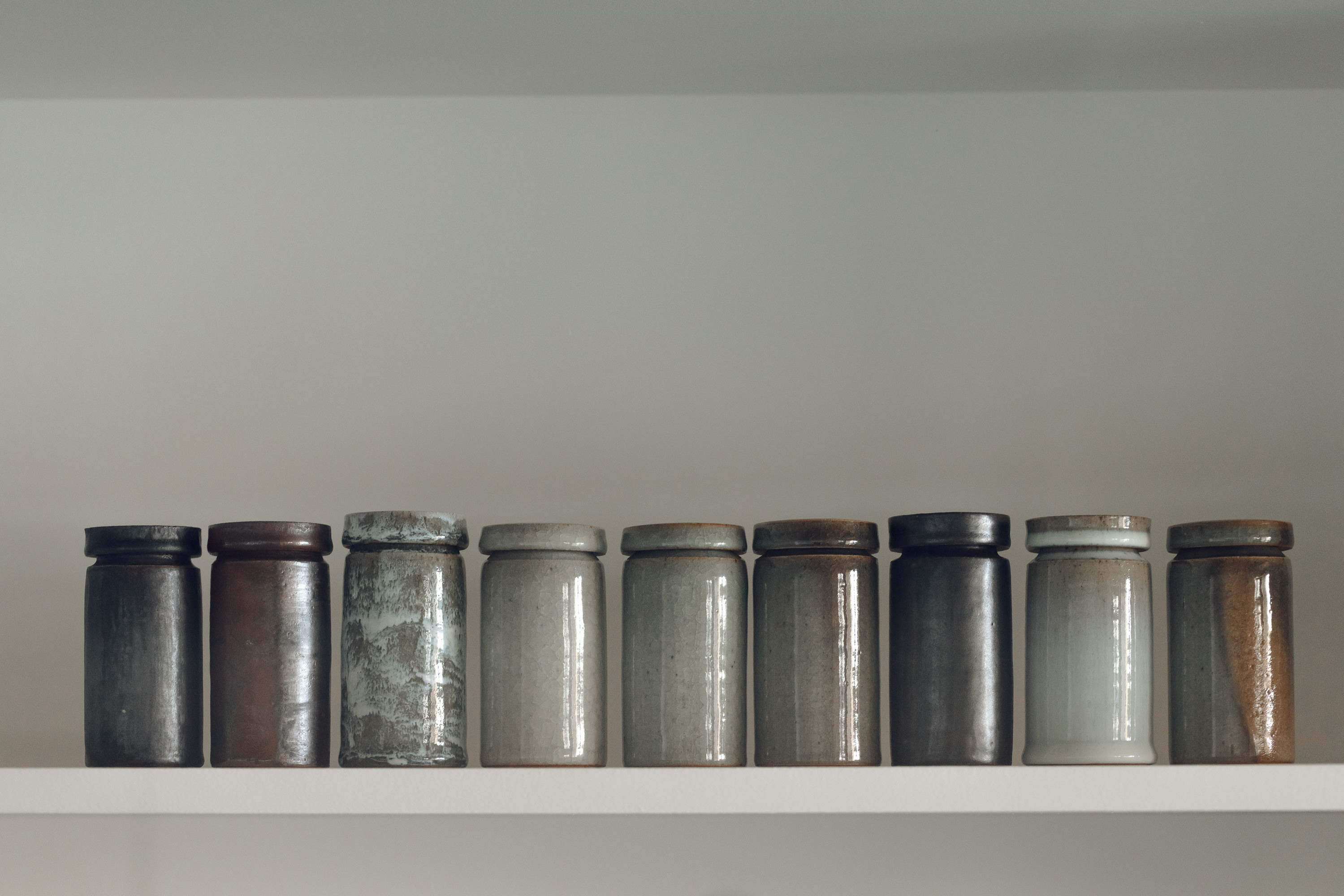 Nine lidded ceramic pots on a shelf