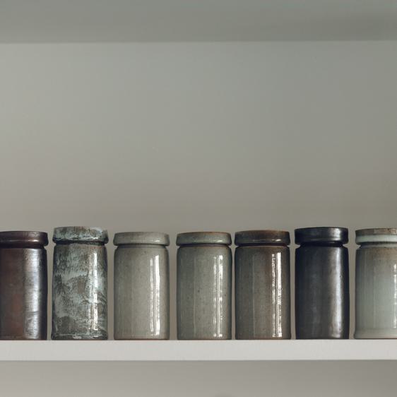 Nine lidded ceramic pots on a shelf
