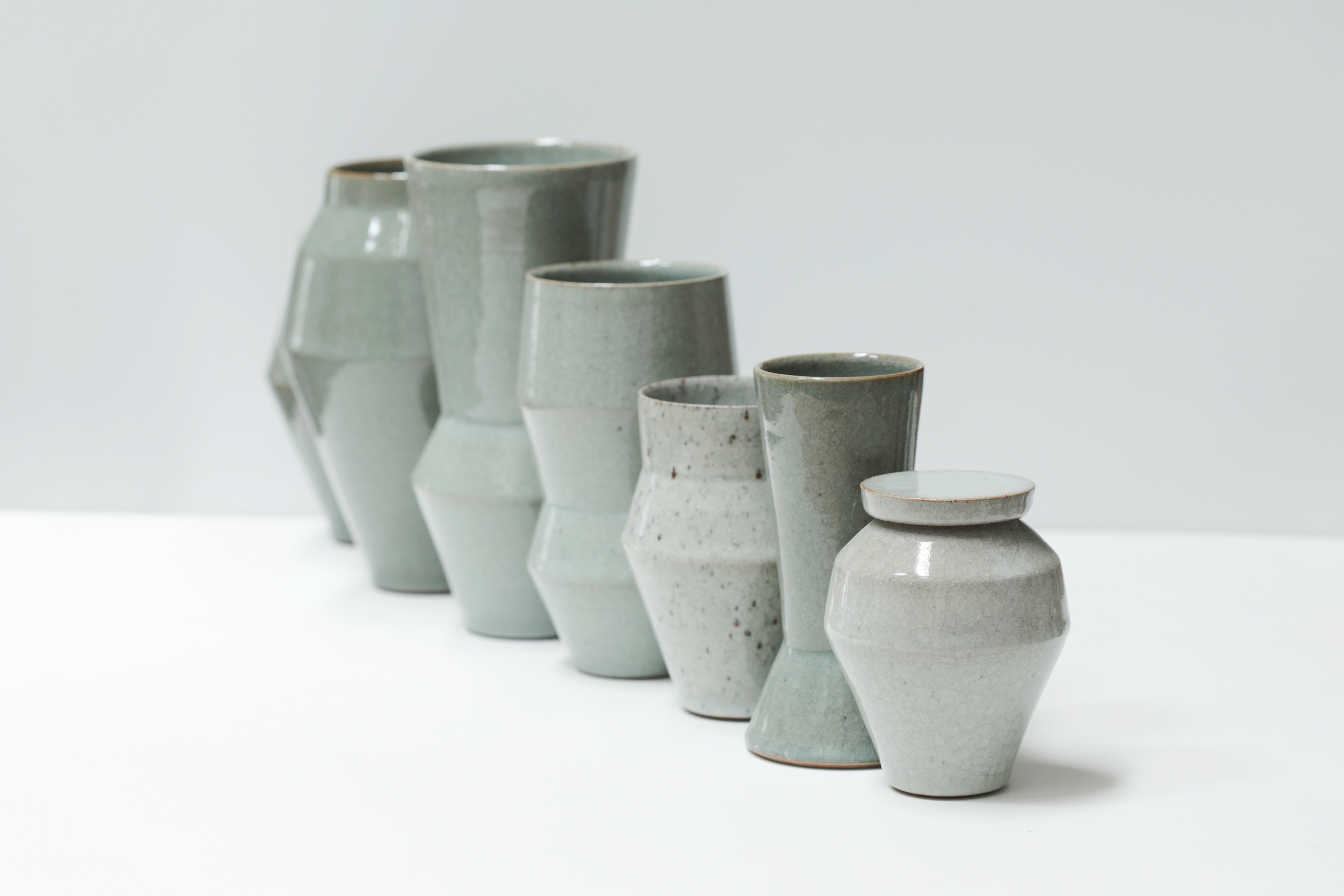 Six green-toned ceramic vases and lidded pots in a row