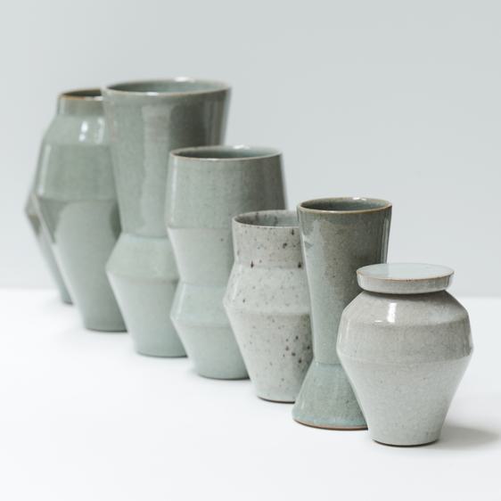 Six green-toned ceramic vases and lidded pots in a row