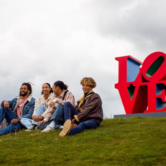 Four friends chatting in front of a red sculpture that reads LOVE