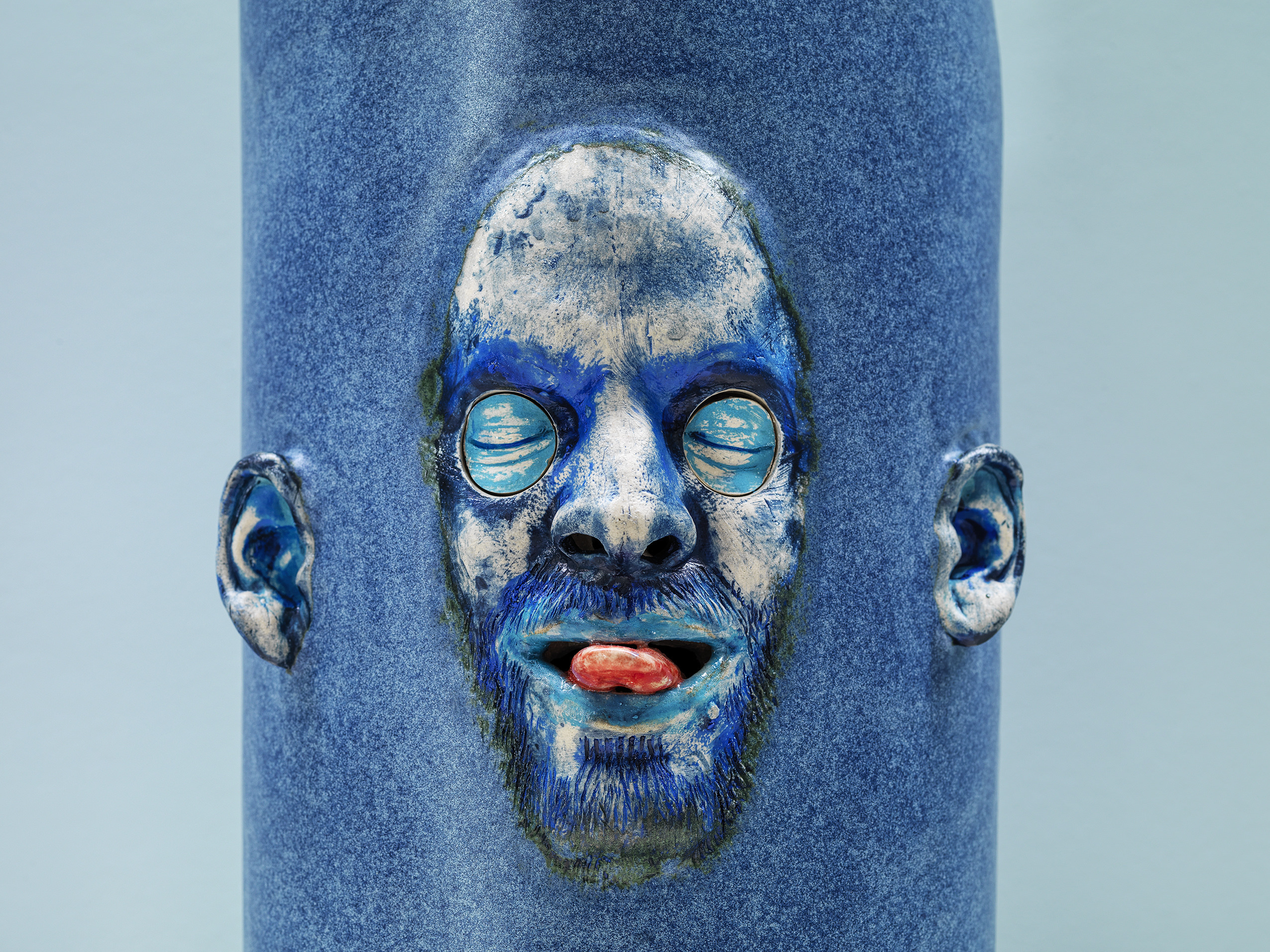 Close up of a blue sculpture of a face with their eyes closed and sticking out their tongue