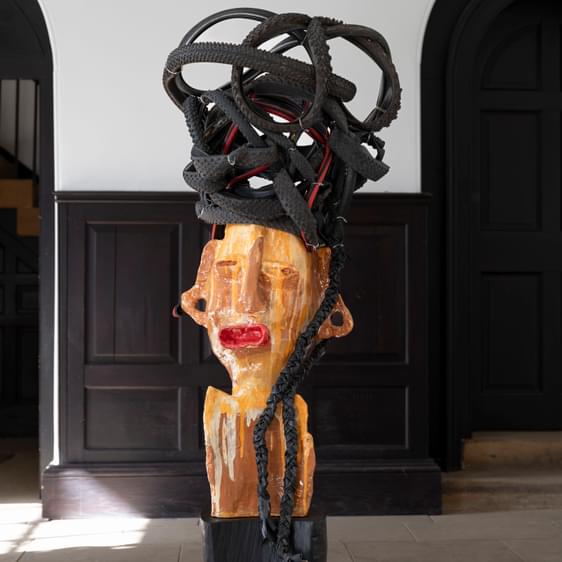 A orange ceramic face sculpture with bike tyres formed on top to look like hair