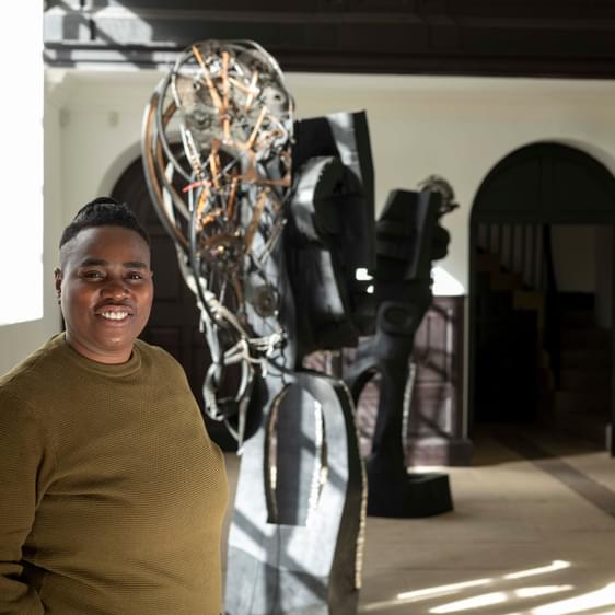 A woman wearing a green jumper standing in front of a large sculpture.