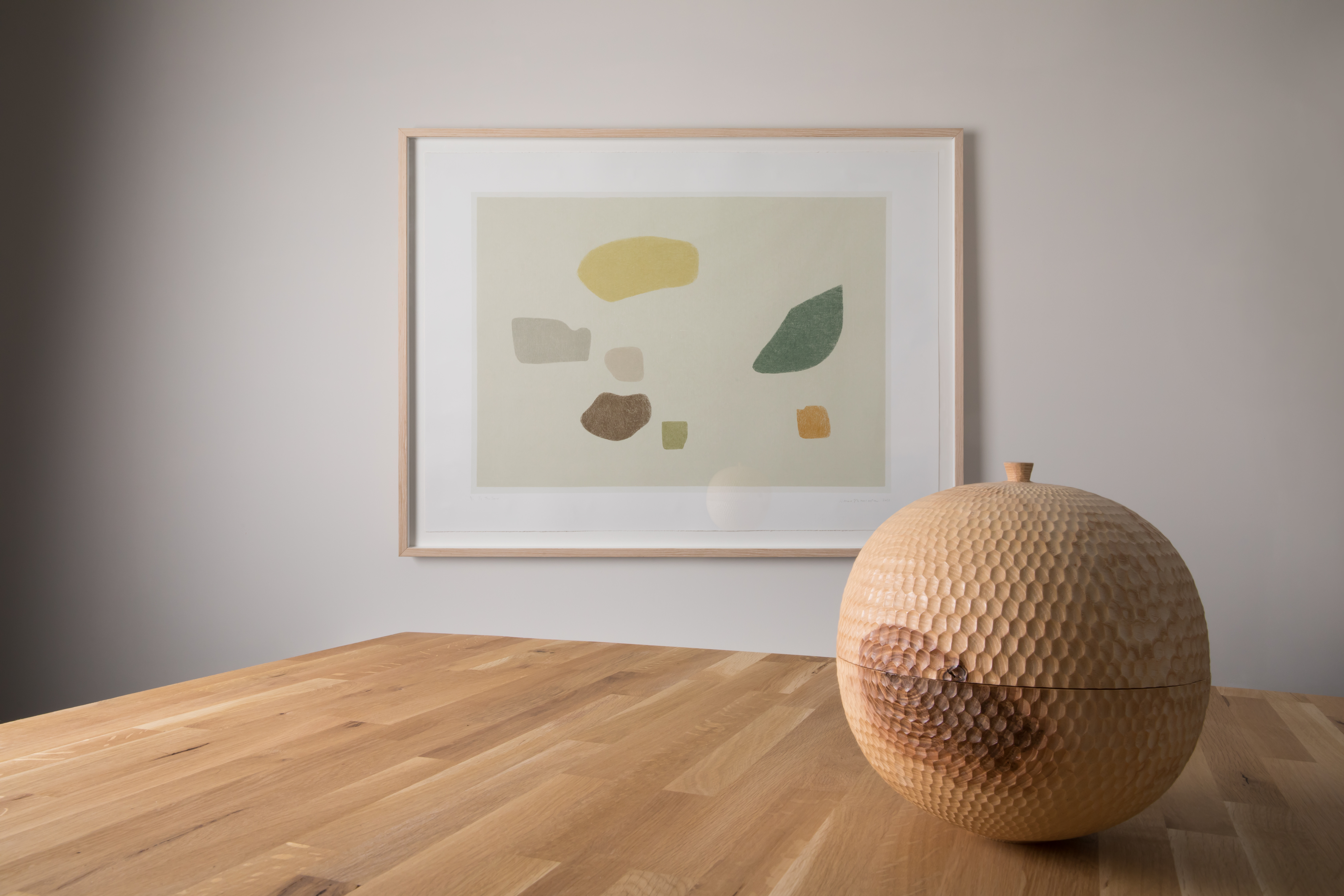 A framed print hung on a wall and a carved wooden vessel in the foreground.