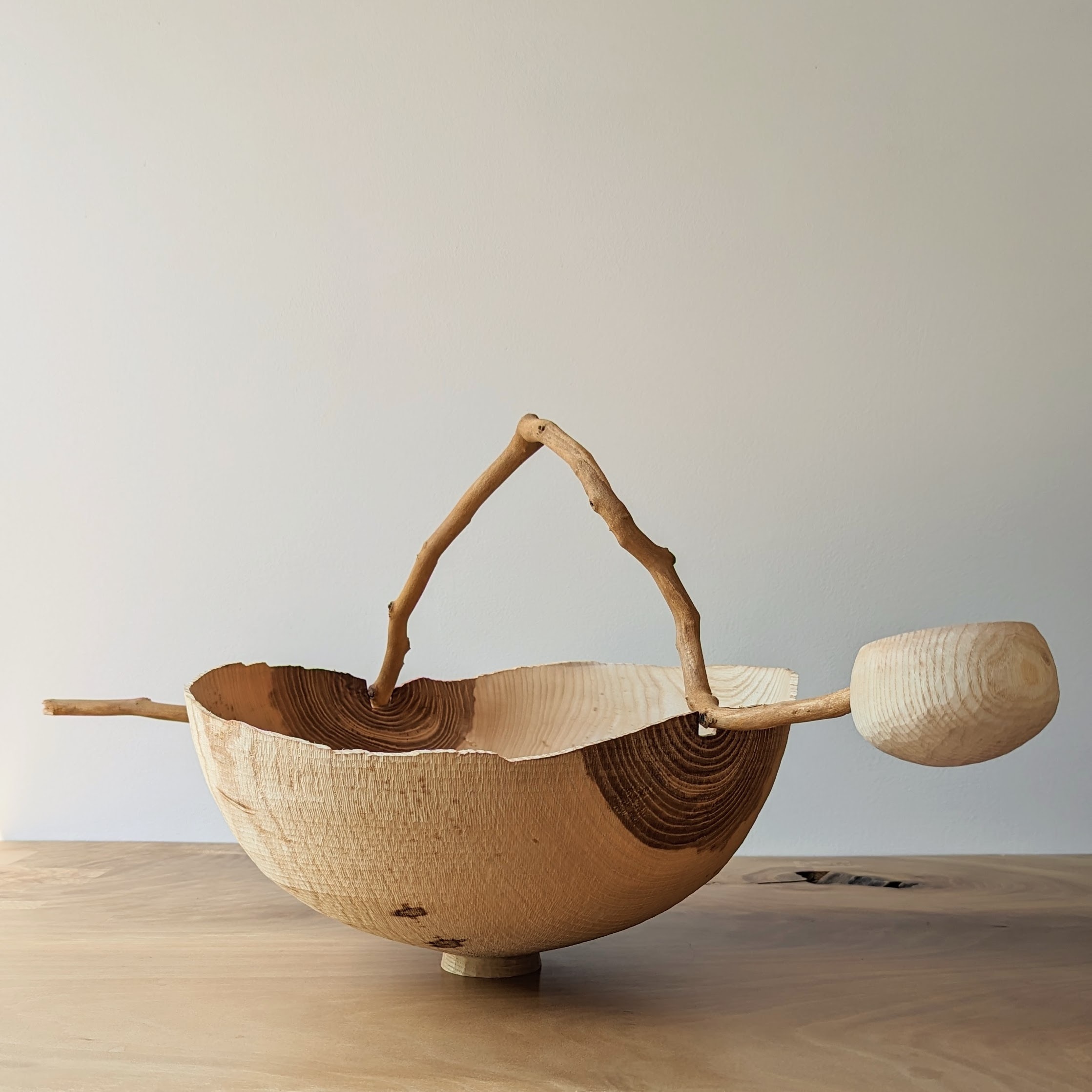 Wooden vessel with a oversized, twig spoon perched on the rim.