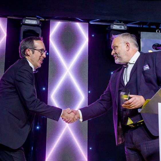 Man holding a trophy shakes the hand of another man wearing glasses.