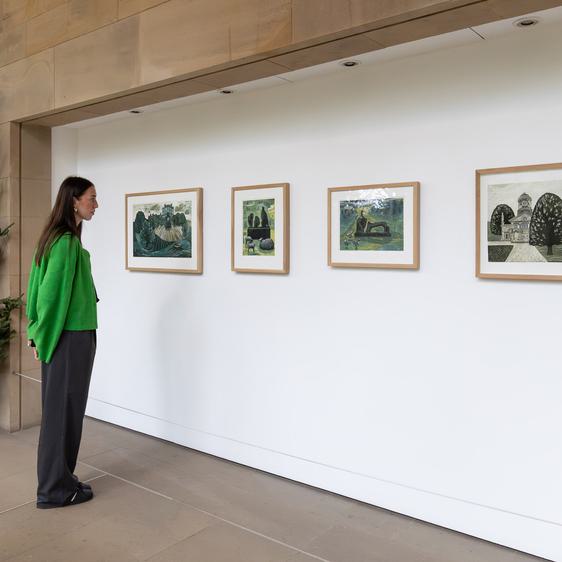 A woman in a green jumper looking at four framed prints on a white wall. A Christmas tree is at the left hand side.