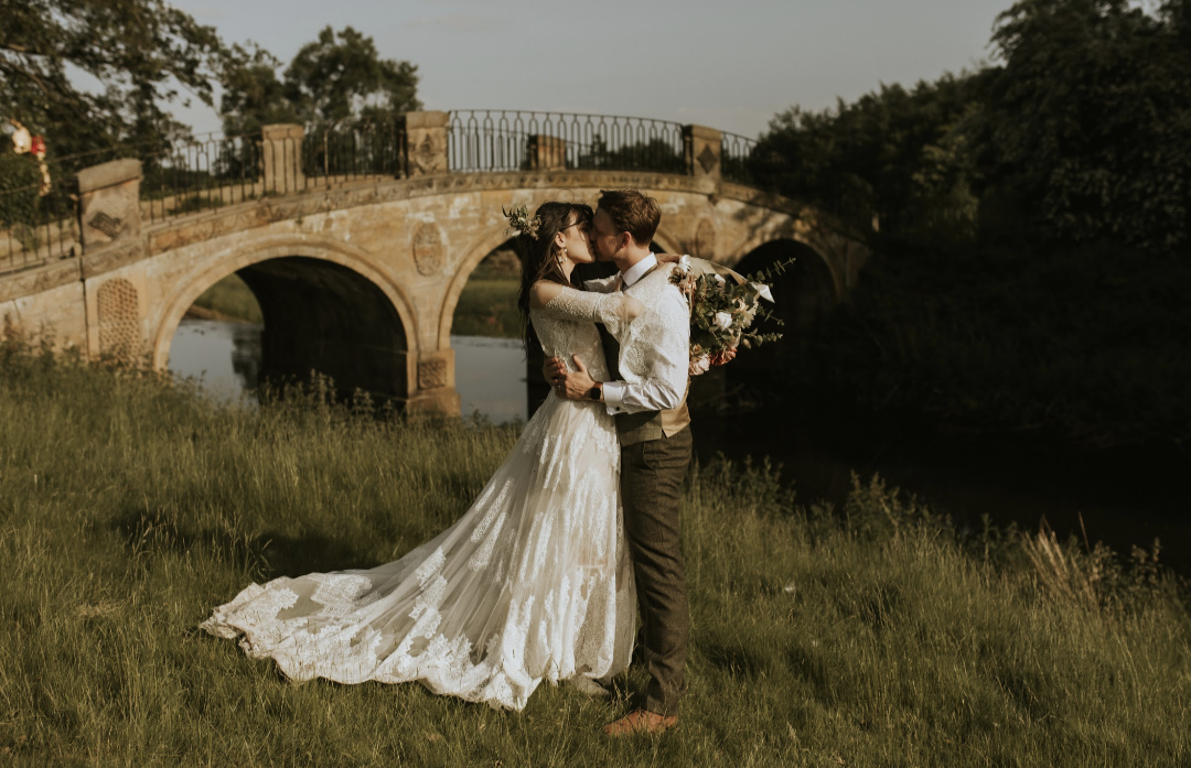 A bride and groom kissing in front of a hump-back bridge