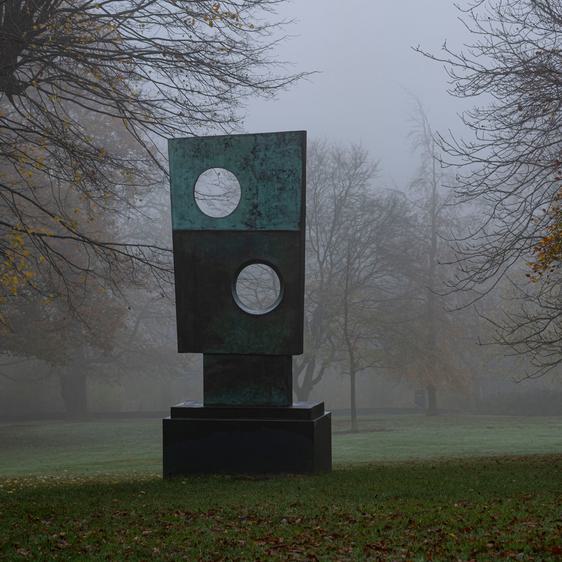A rectangular sculpture with circular cut outs, displayed outdoors on a foggy day.