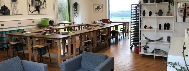 A studio space with rows of tables and comfy chairs, with artworks displayed on the walls.