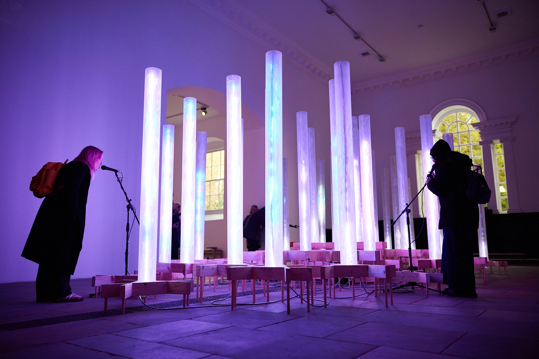 Two adults singing into microphones surrounded by glowing columns.