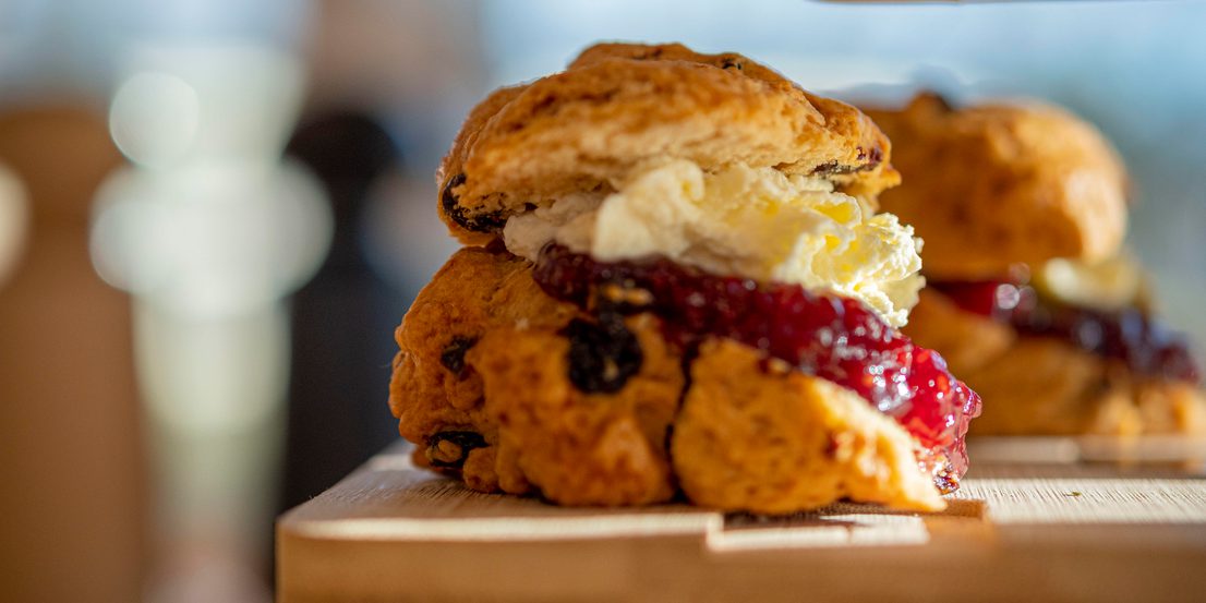 A scone filled with cream and jam on a wooden board