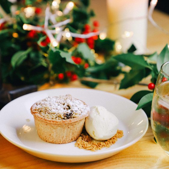 A plate of mince pies and cream, surrounded by festive foliage
