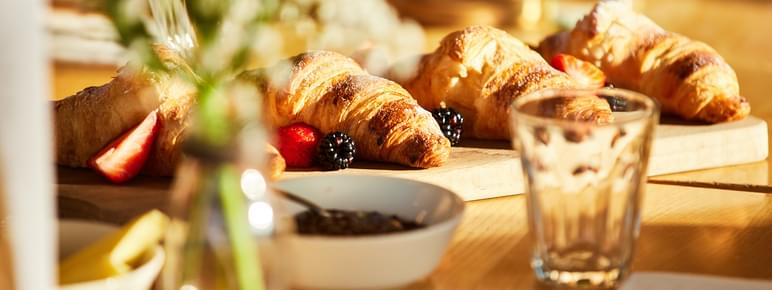 A board of croissants with fruit and water glasses on a table.