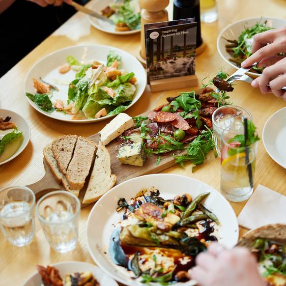 A table filled with small plates of food while hands holding forks reach for the food.