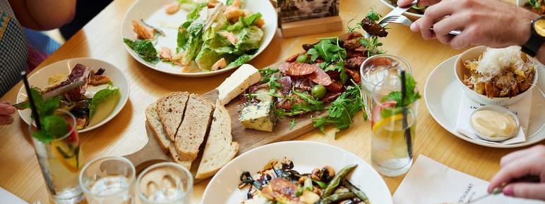 A table filled with small plates of food while hands holding forks reach for the food.
