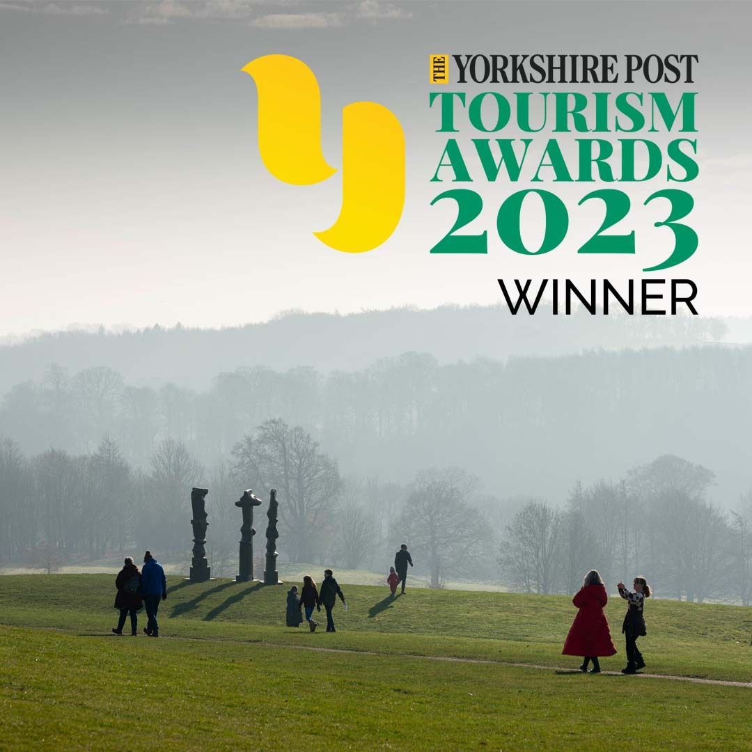 People walking across a hillside, with three tall thin silhouetted sculptures and trees in the background. The Yorkshire Post Tourism Award 2023 Winner logo is in the top right corner.