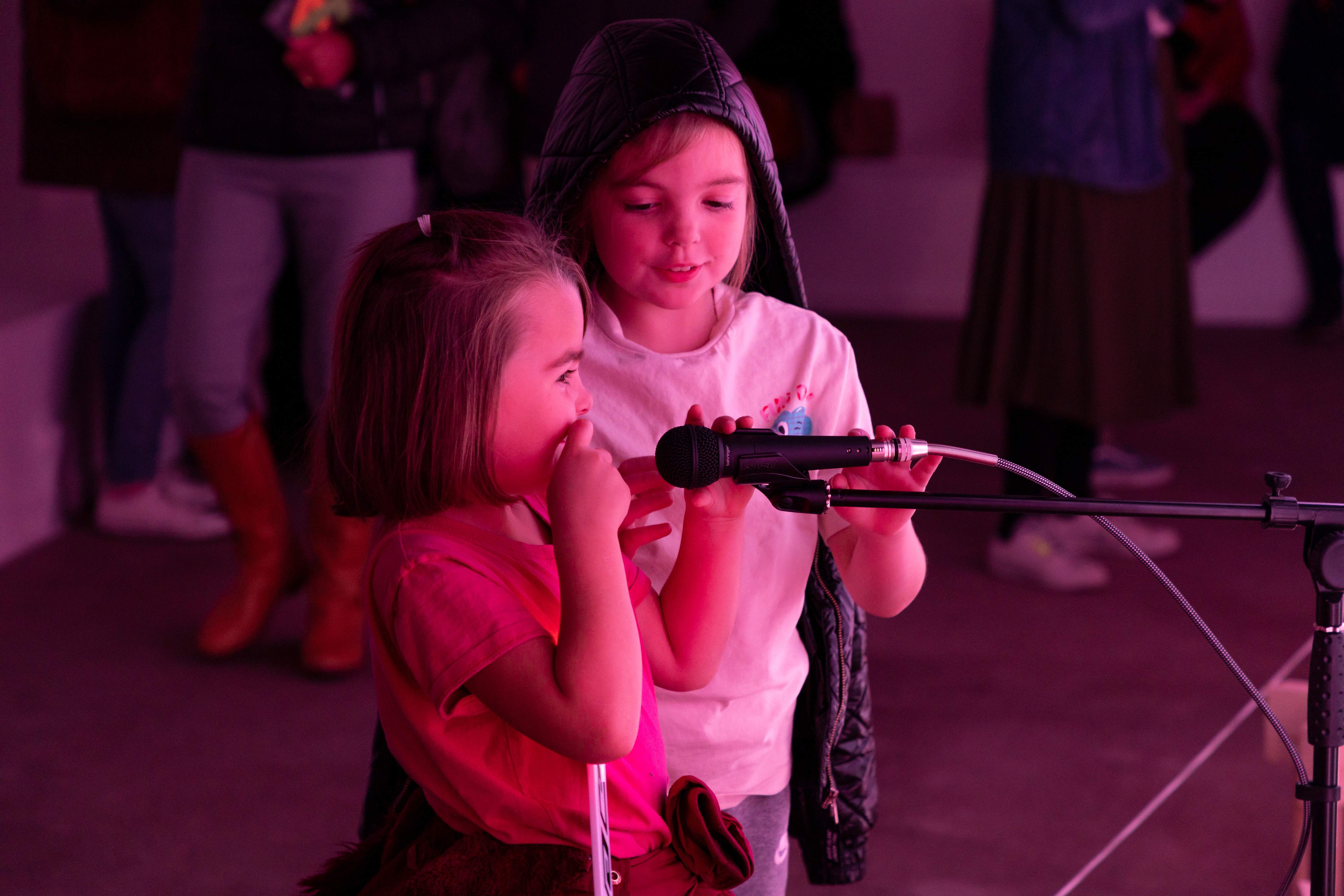 Two children making sounds into a microphone, surrounded by pink light