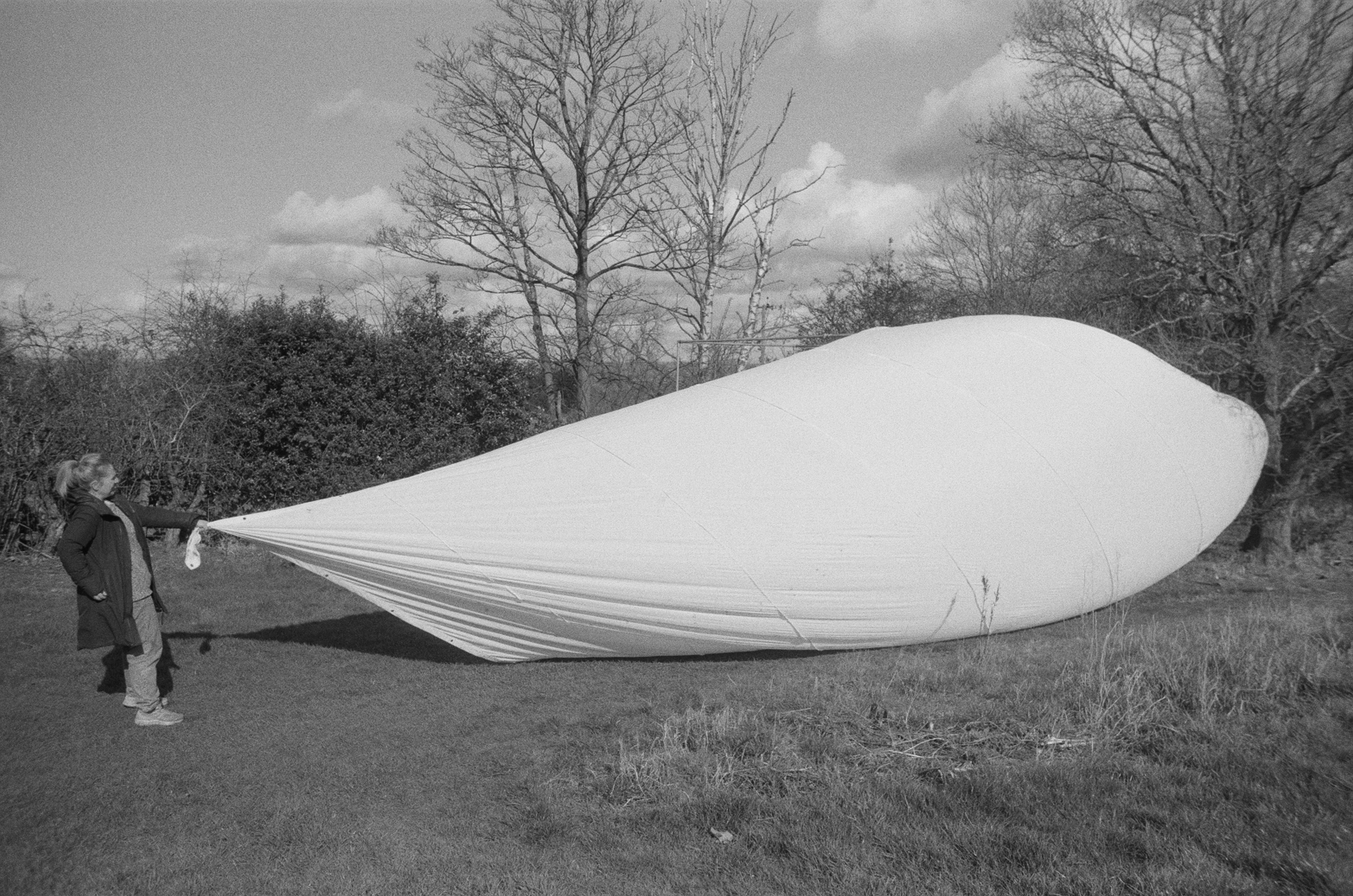 A woman holding the end of a large white piece of fabric which is filled with air like a balloon.