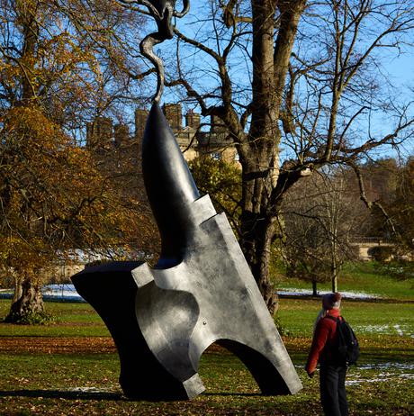 A woman looking at a sculpture of a hare balanced on the tip of an oversized anvil, displayed outdoors.