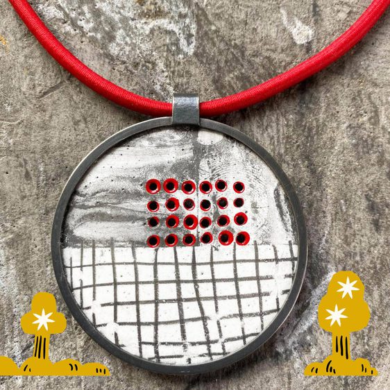 Detail of a circular enamel necklace pendant, in shades of white, black and red, on a red cord.