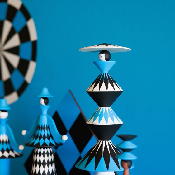A vibrant blue wall serves as the backdrop for a collection of wooden figures, featuring geometric patterns in black and white.