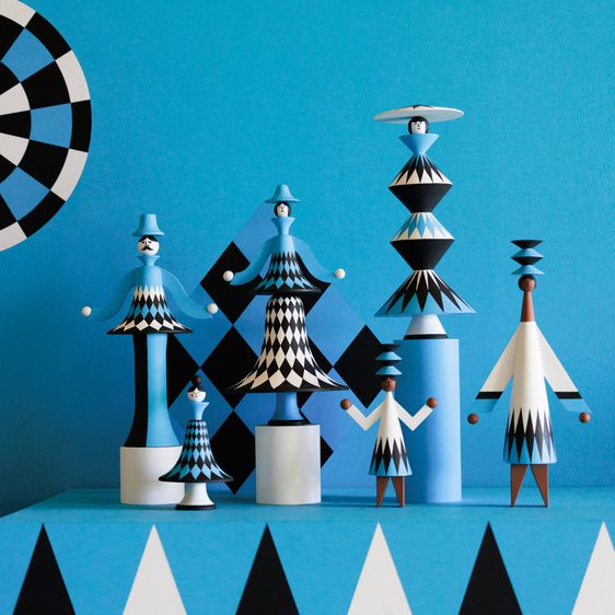 A collection of whimsical wooden figurines in various shapes and sizes, featuring a vibrant blue background with geometric patterns. The figures are painted in shades of blue, black, and white, showcasing playful designs and a circus theme.