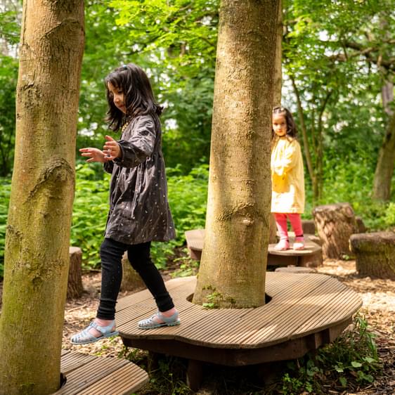 Two children jumping between wooden platforms in a nature play area.