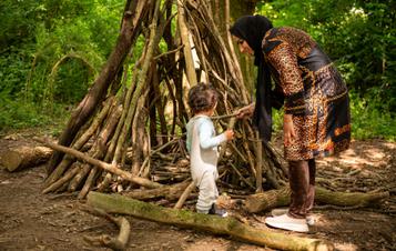 A toddler and adult building a den out of sticks
