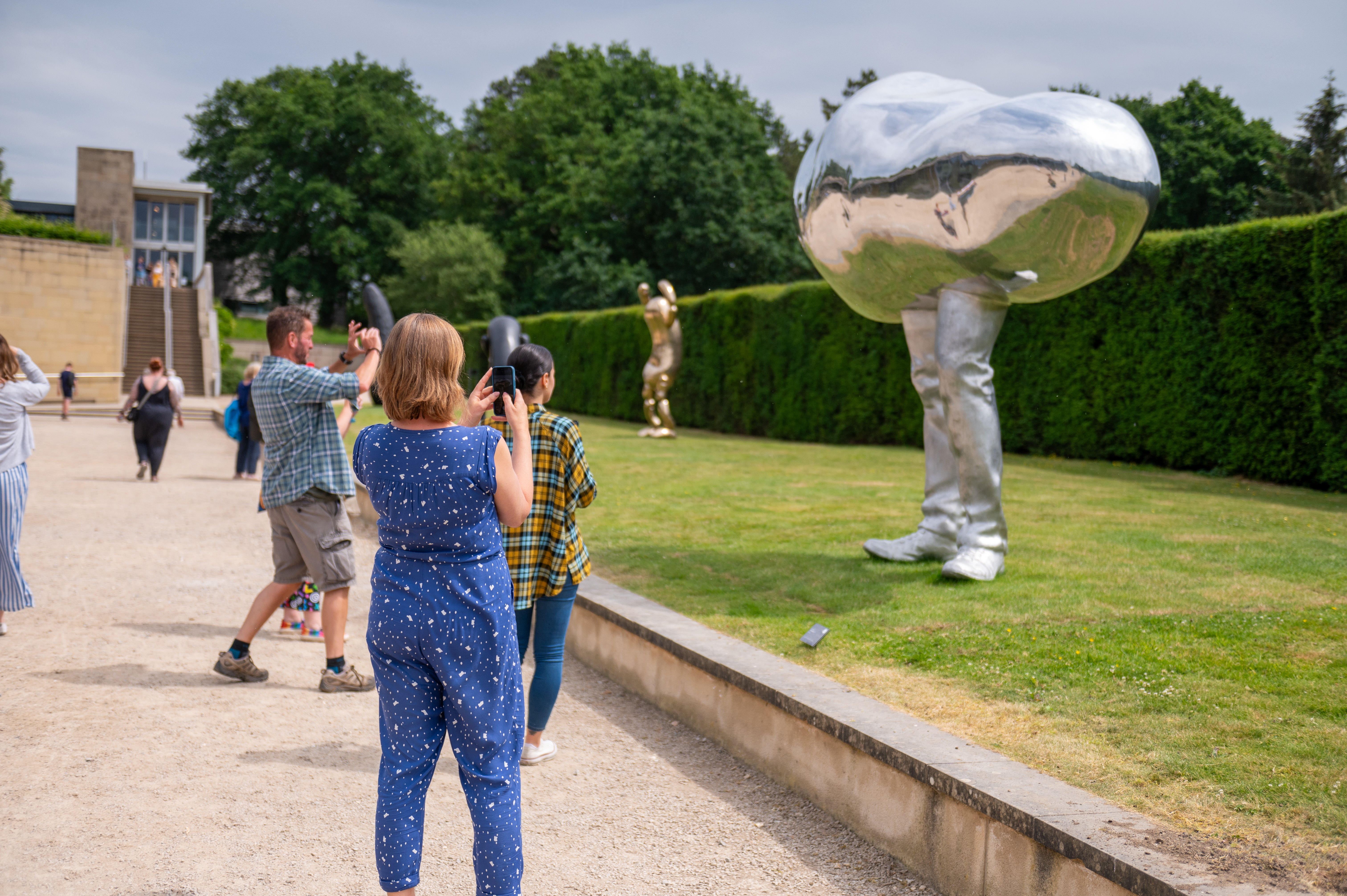 A group of people taking photographs of an oval silver sculpture with legs.
