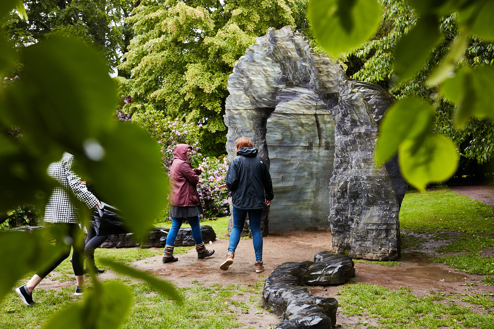 Three people in rain coats looking at an igloo-like sculpture