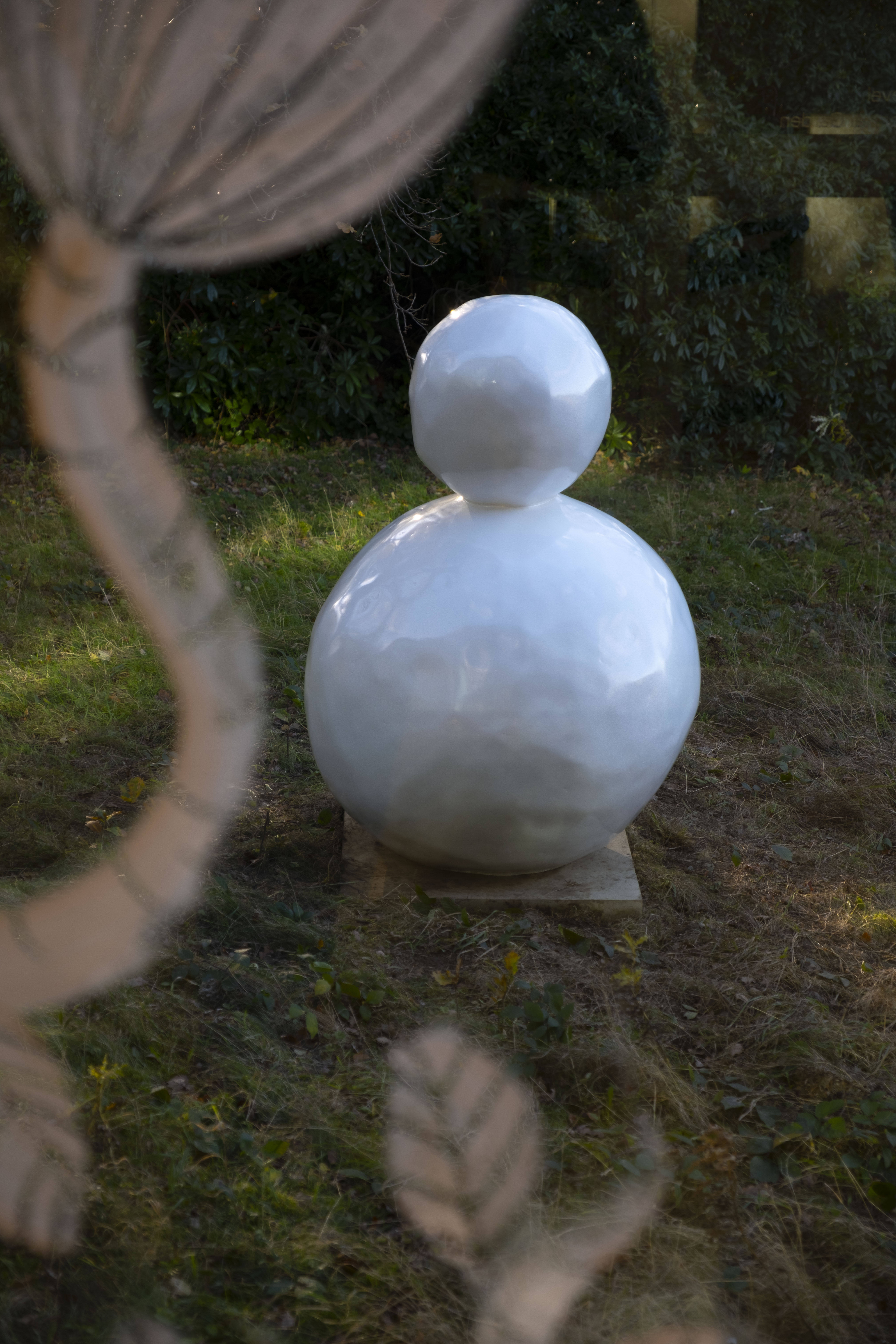A white snowman sculpture, with trees and a while flower shaped sculpture behind it.