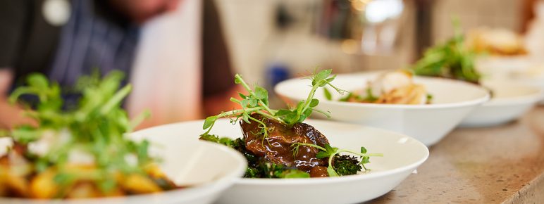 A row of dishes on a counter full of food. The chef is in the background.