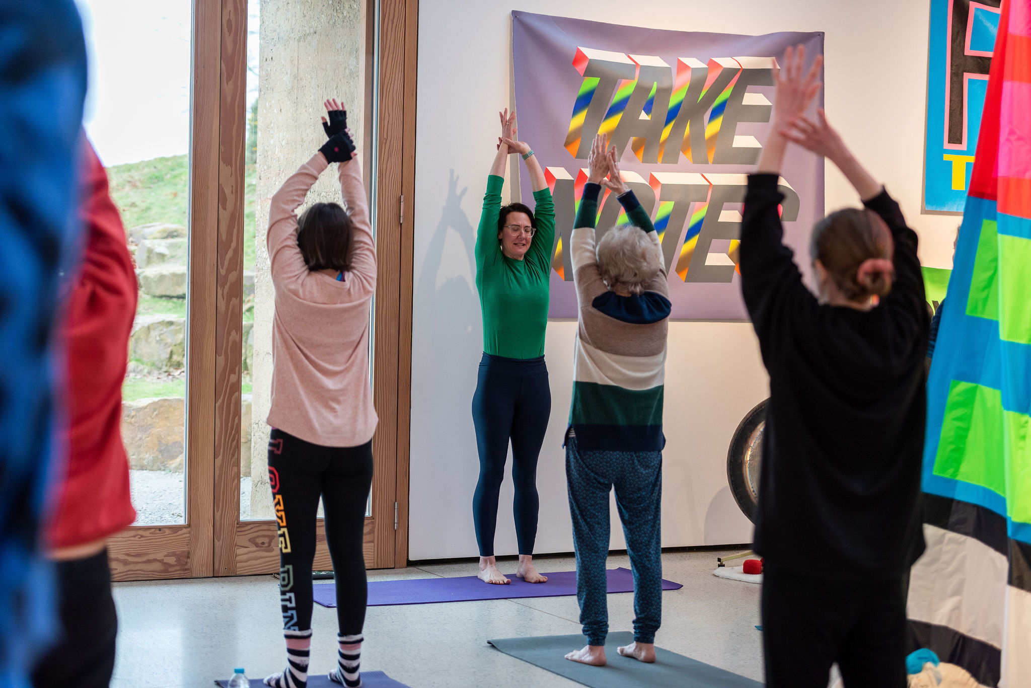 A group of people practicing yoga in a gallery space, surrounded by colourful fabric hangings.